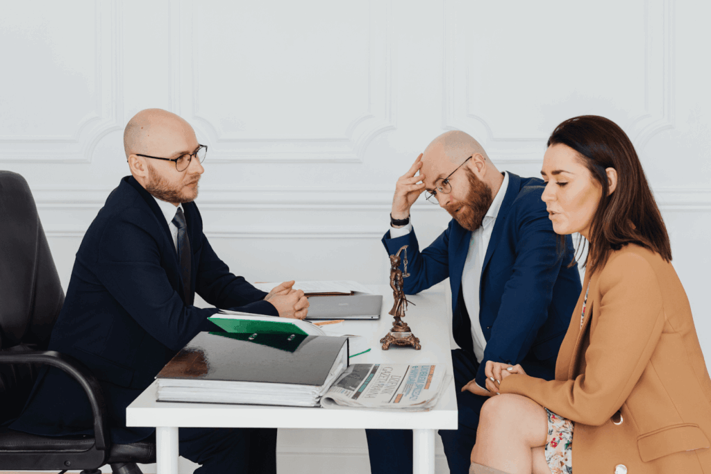 Divorcing couple sitting with their lawyer at a desk discussing legal documents and settlement options during a divorce consultation.