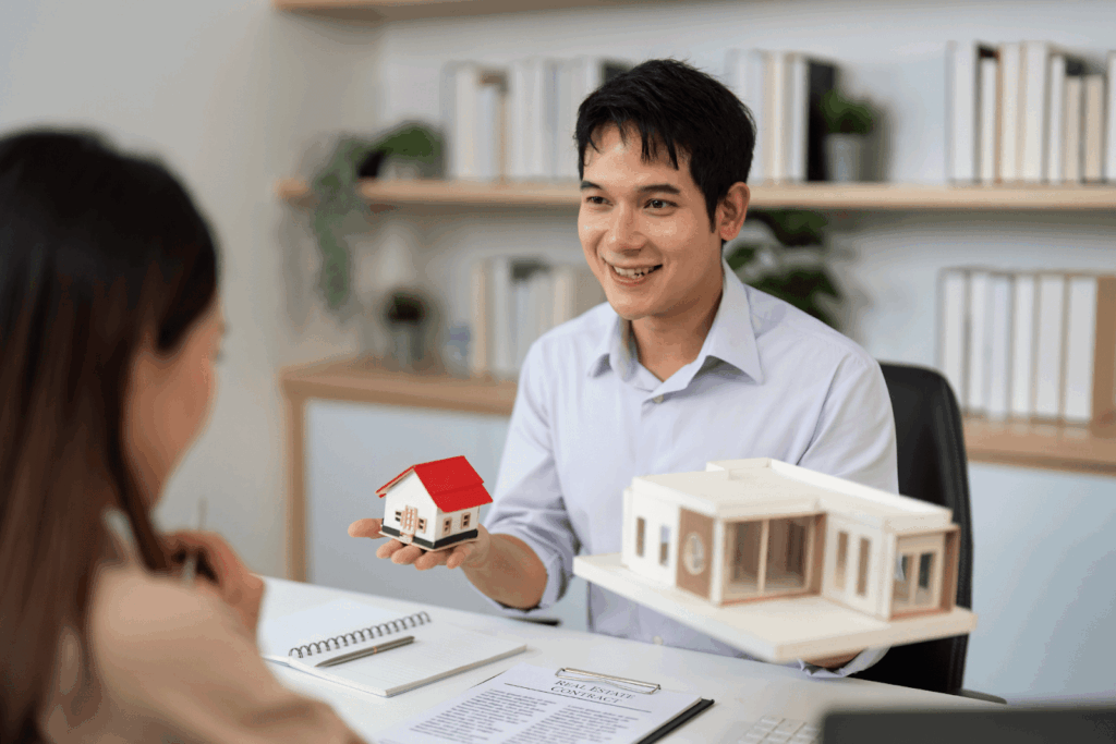 Real estate agent showing a small model house to a client during a meeting about selling or purchasing rental property.