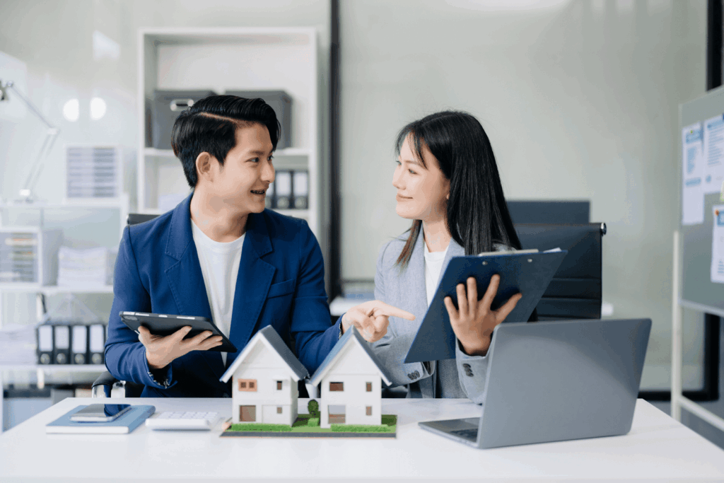  Two real estate professionals reviewing documents and house models while discussing a property sale.
