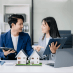 Two real estate professionals reviewing documents and house models while discussing a property sale.