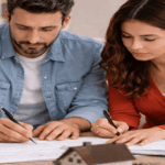 Married couple reviewing and signing house documents with a small home model on the table while discussing property decisions during a divorce.