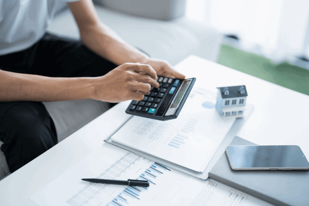 Homeowner using a calculator to review mortgage payments and financial documents with a small house model on the table.