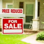 Real estate for sale sign with price reduced notice in front of a residential home.
