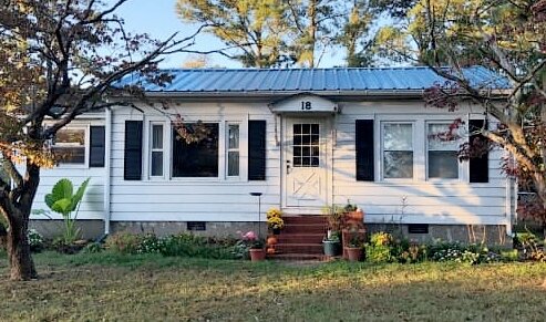 Small fixer-upper ranch-style house on a sunny day surrounded by trees.