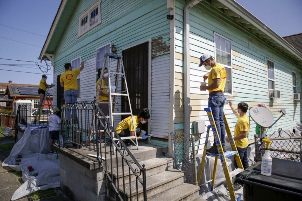Group of men in yellow t-shirts repairing and painting a house in green color on a sunny day in Chesapeake VA