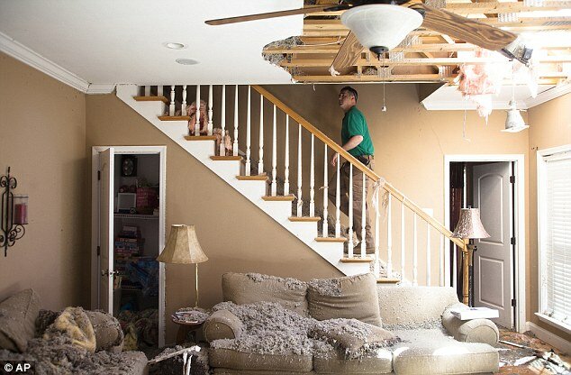House damage inside a room, with a man walking up a stairwell in a green shirt.