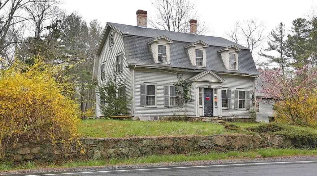 Two story visually distressed house with white siding and small green grass yard.