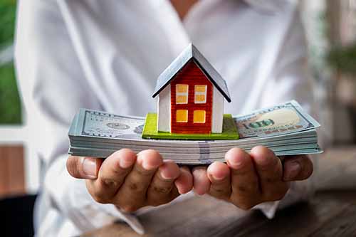 Hands holding stack of money with model house on top