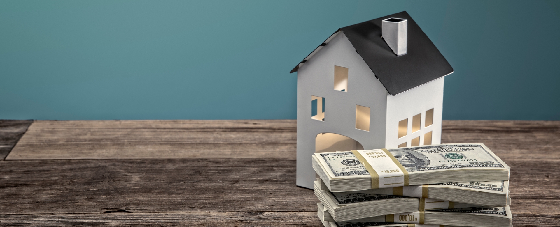 Model house on a wood table next to a stack of money.