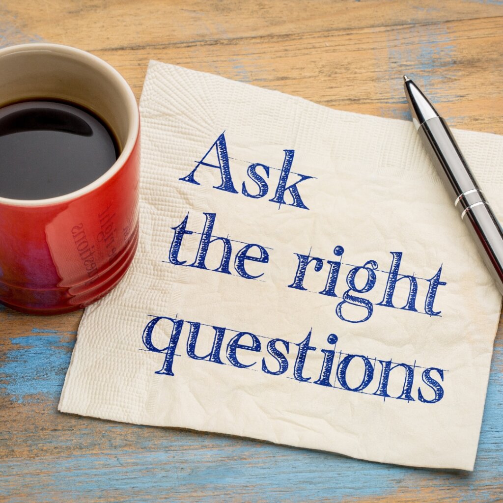 Table top with red mug of coffee, a pen, and a napkin with "ask the right questions" written on it.