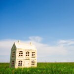 Tiny white model house on green grass with open sky