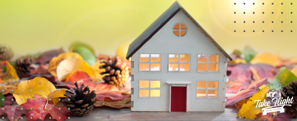 Model house on wood tabletop with autumn leaves and pinecones