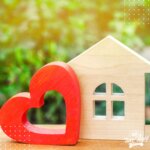 Artistic image; Small model wooden house model with red wooden heart, greenery and sunlight in the background