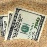 Three $100 bills sinking in sand.