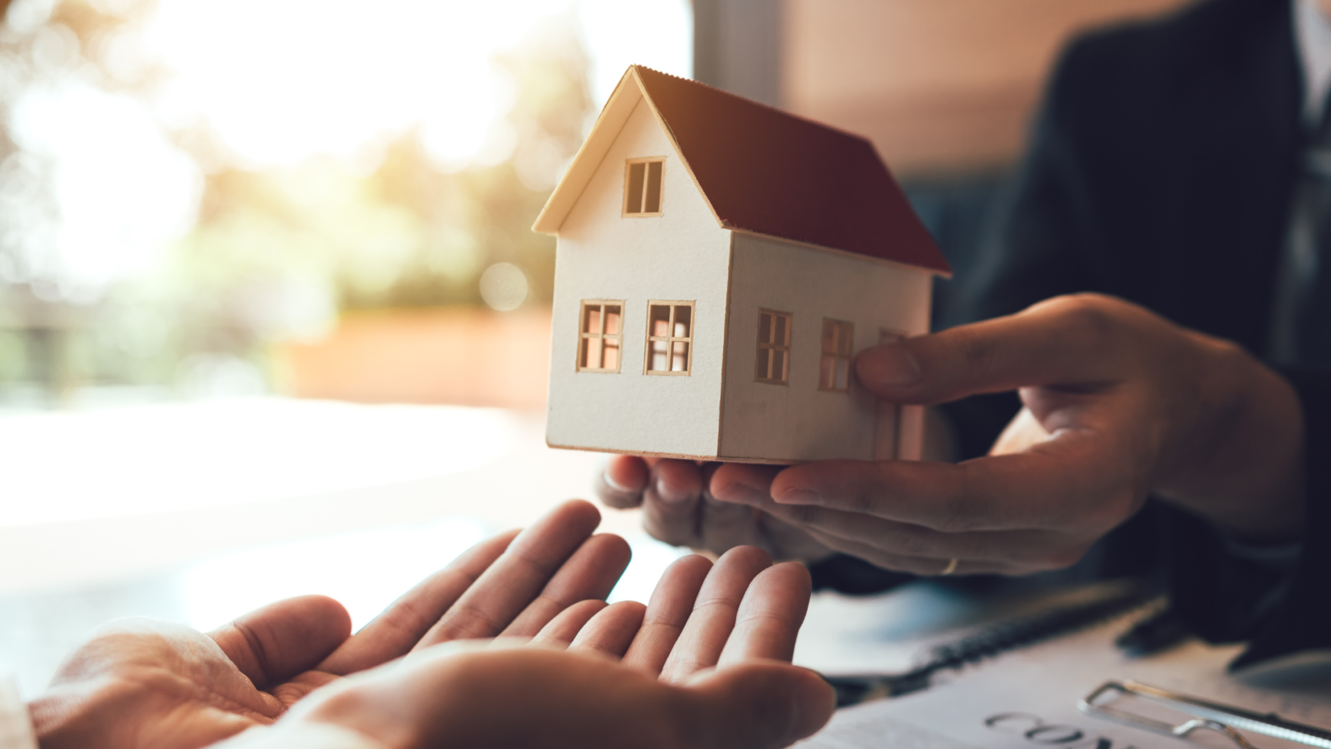 Hands turning over a small house from buyer to seller