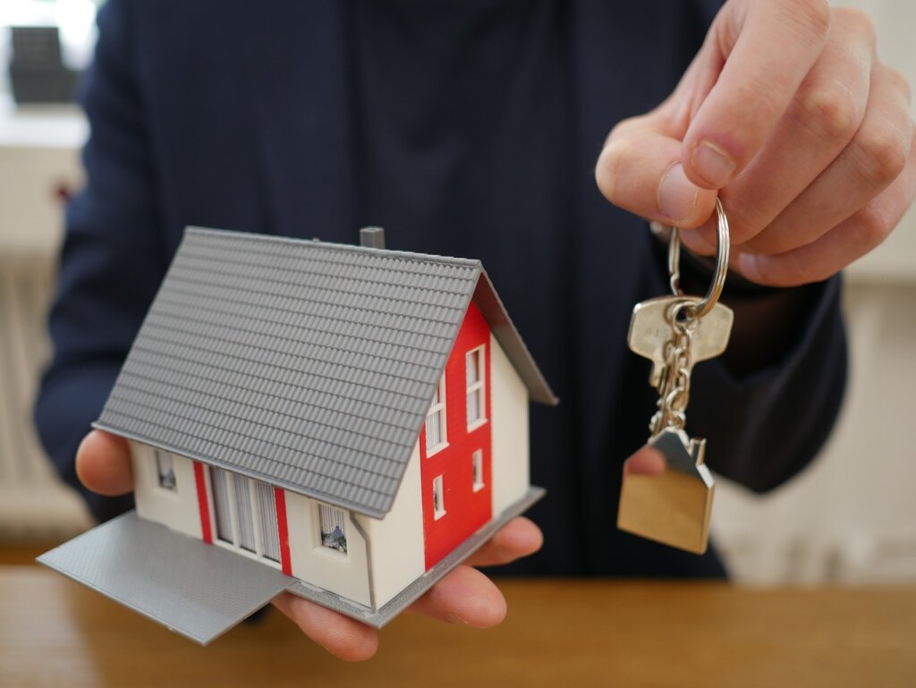 a man holding a small house and the keys