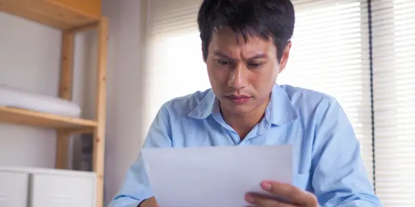a man looking worried as he reads a foreclosure notice from his lender
