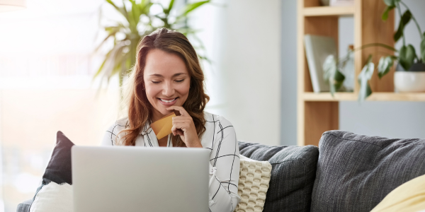 A woman sits comfortably on a couch, working on her laptop with a relaxed expression