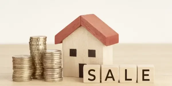 wooden miniature house with coins and a spelled out "sale" in a word block