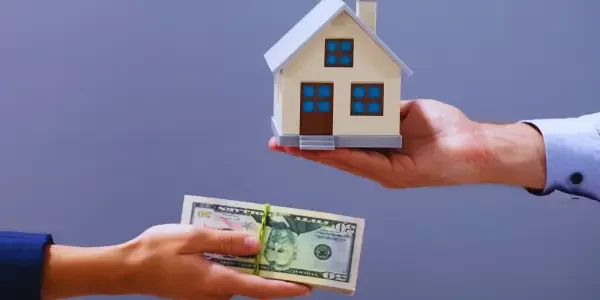 Two hands exchanging: one holding money, the other a miniature house.