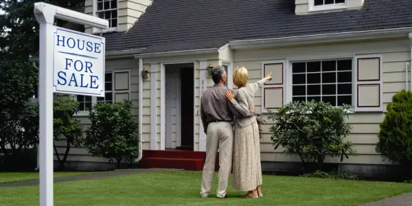 a couple standing in front of their house that is up for sale