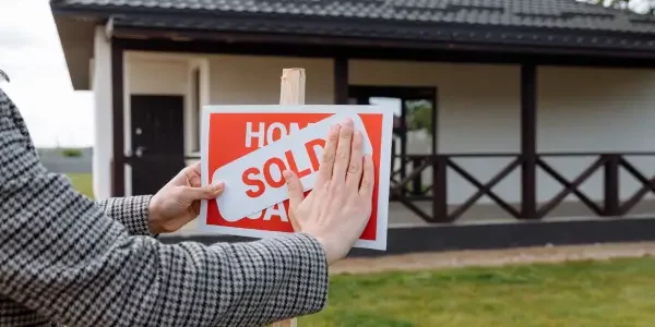 a person putting a sold sign over the "house for sale" sign