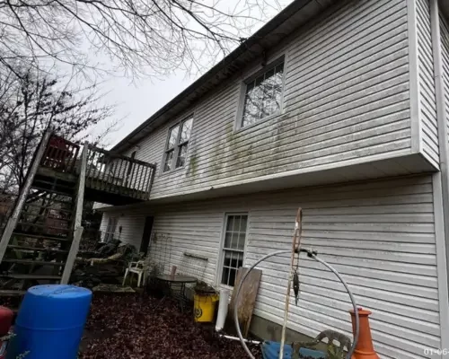 Back side of the house showing worn out walls and wooden backyard stairs