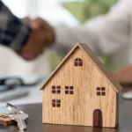 A wooden tiny house with 2 peoples shaking hands in the background
