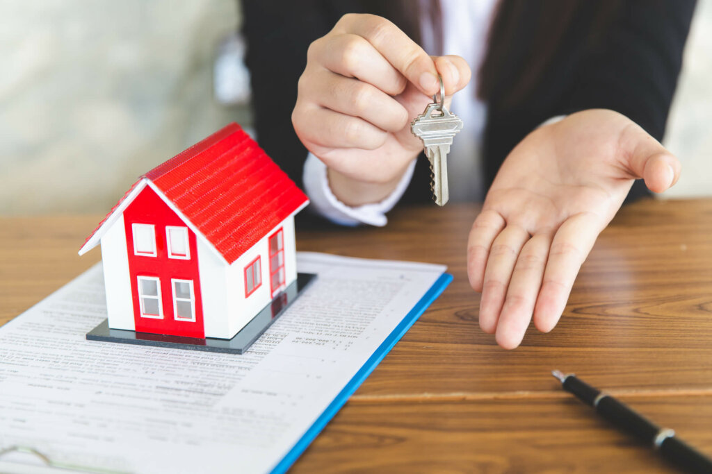 Learn how to sell your Illinois home fast Person holding Illinois house key next to a model house and gesturing in a manner that suggests selling a house.