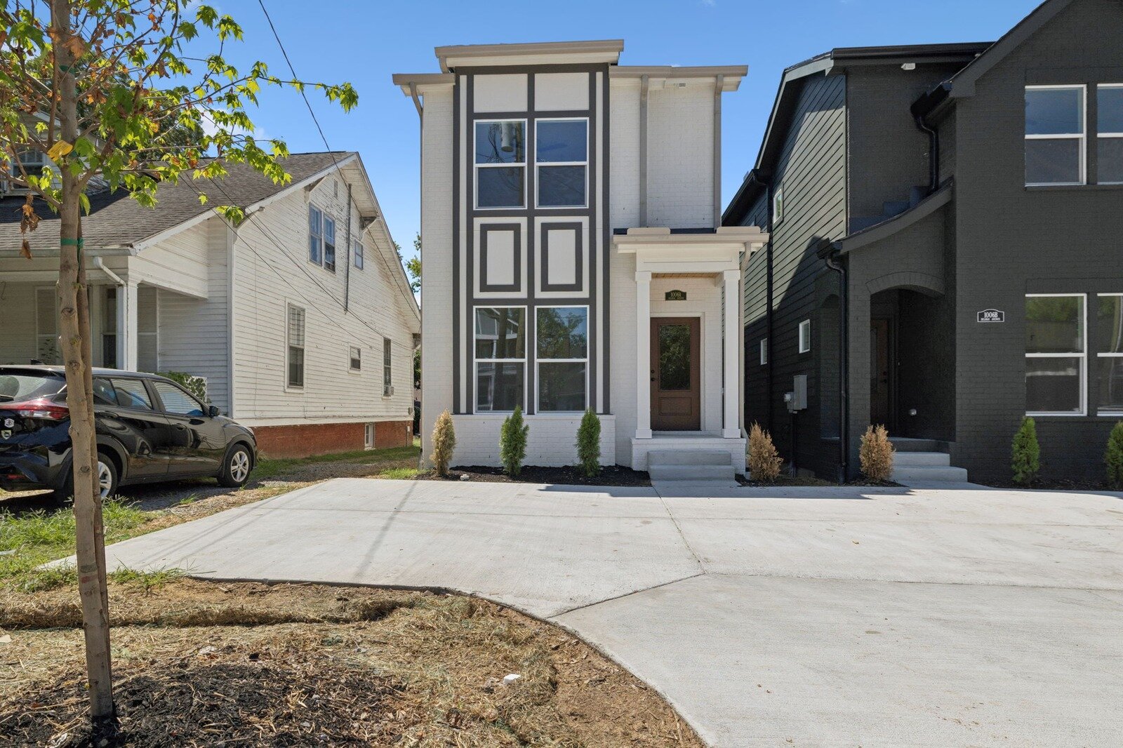 Modern white new-construction home on an infill lot beside an older cottage in Nashville, Tennessee