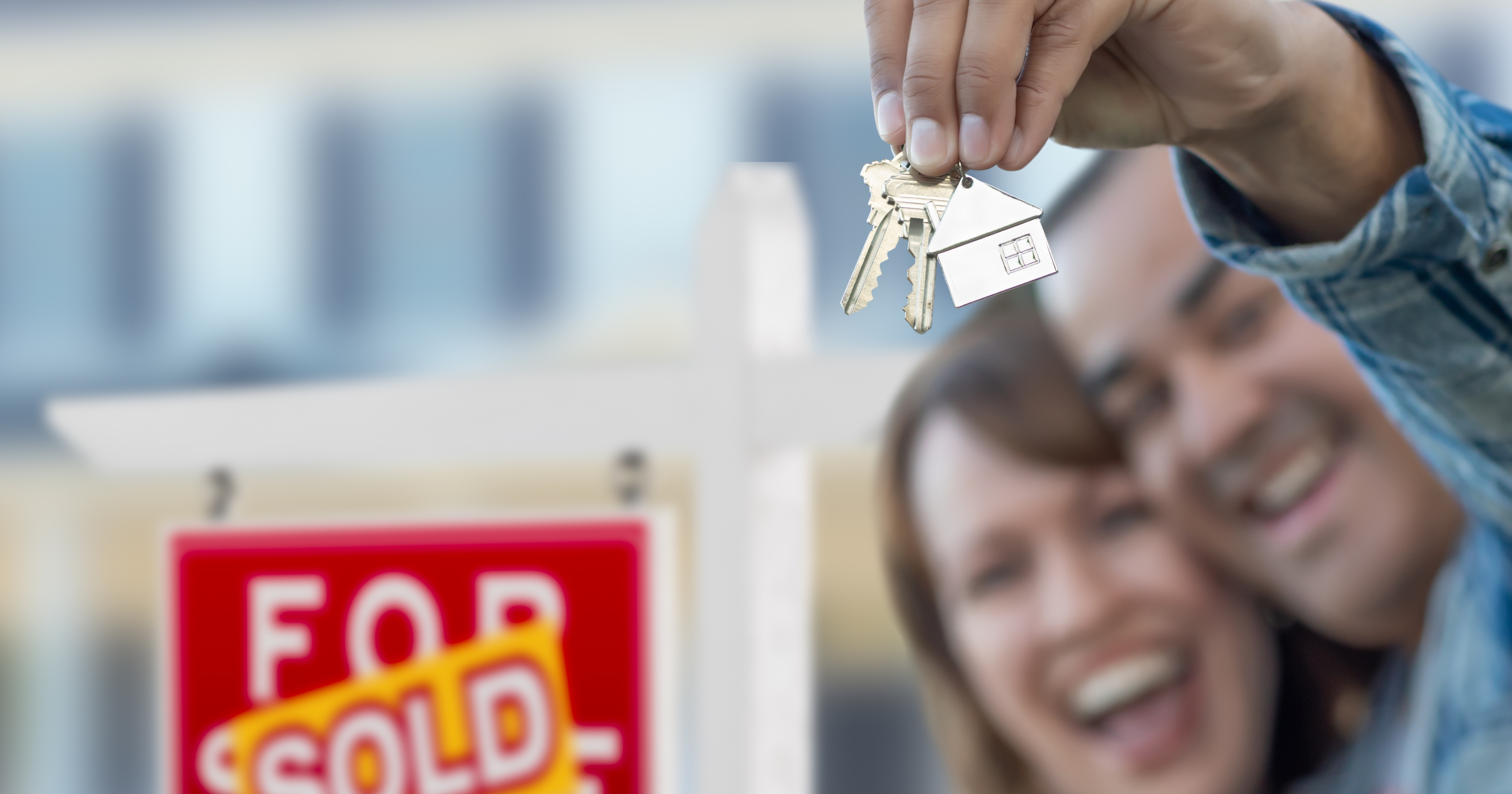 Happy homeowners holding keys in front of a 'Sold' sign, symbolizing the ease of selling your inherited property quickly and stress-free with REvitalize Property Solutions.