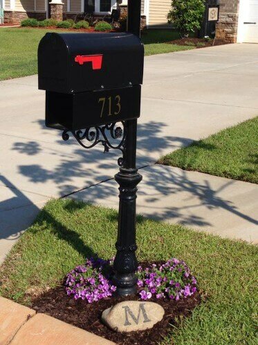 Black metal mailbox with purple flowers and large rock with "M" written on it