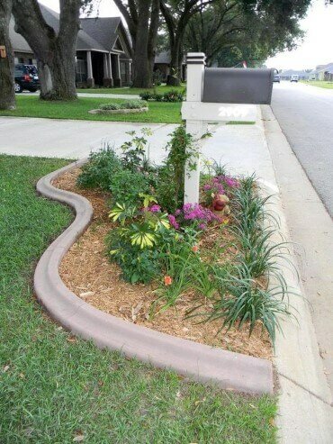 Curvy flower bed with stone edging around the mailbox with many ornamental grasses