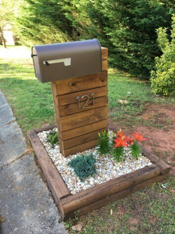 Wood mailbox with gold house numbers sitting in a flower bed with plants and rocks