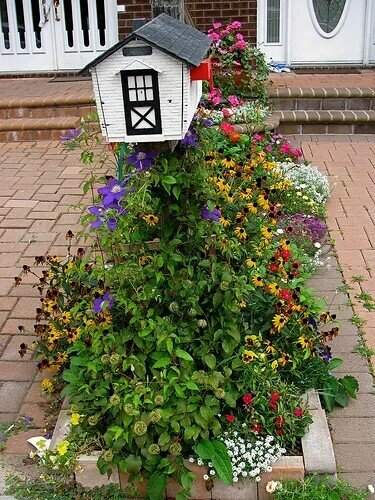 house shaped mailbox surrounded by a variety of colorful flowers