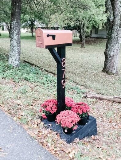 Pink and black mailbox with pink house numbers and pink flowers planted in the flower bed around it