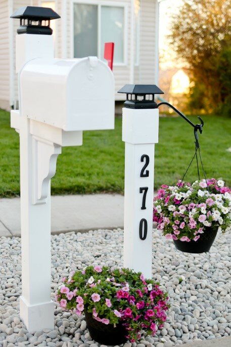 White mailbox next to white post with house number and a hanging planter