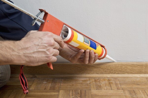 applying caulk between wall and wood trim