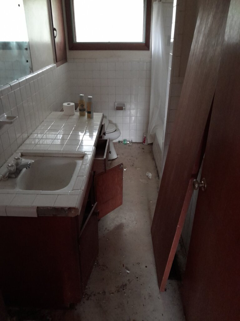 A bathroom that has the trash removed, but needs repairs to the counter and fixtures.