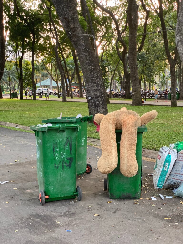 Trash cans on the street with trash in and around the cans.