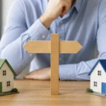 Two model homes separated by a signpost representing different home-buying companies
