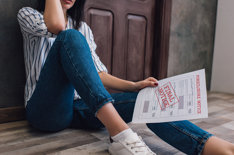 A young woman sitting on the floor of her house holding a final foreclosure notice 