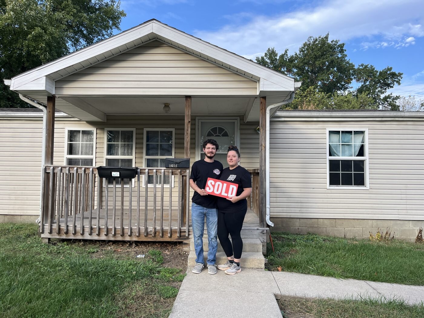 Clients holding a SOLD sign in front of their new home.