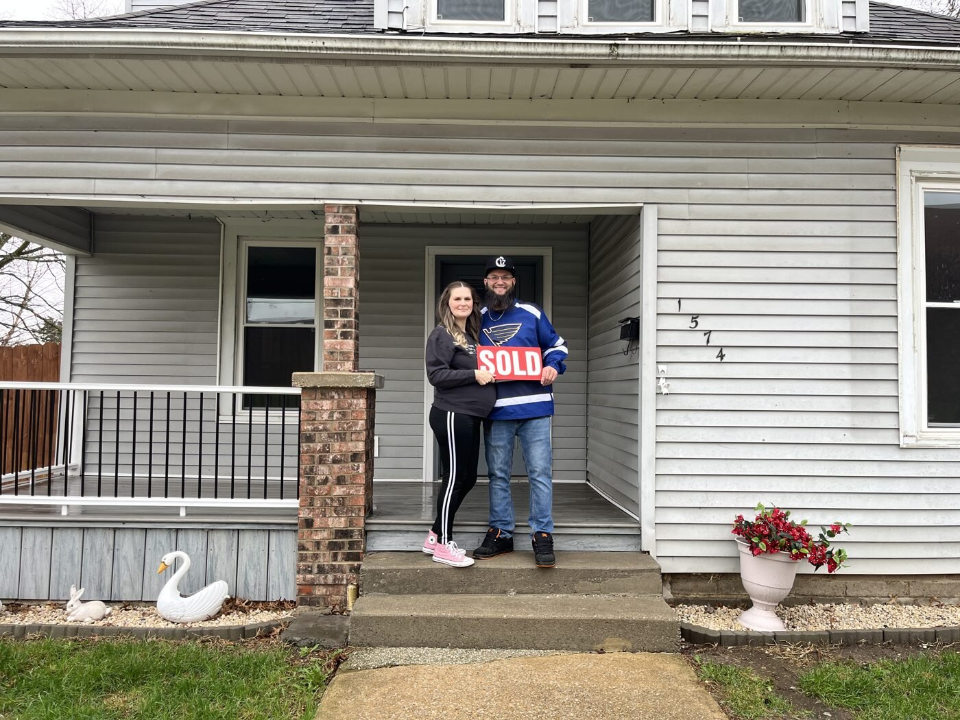 A couple celebrating with a SOLD sign on their front porch.