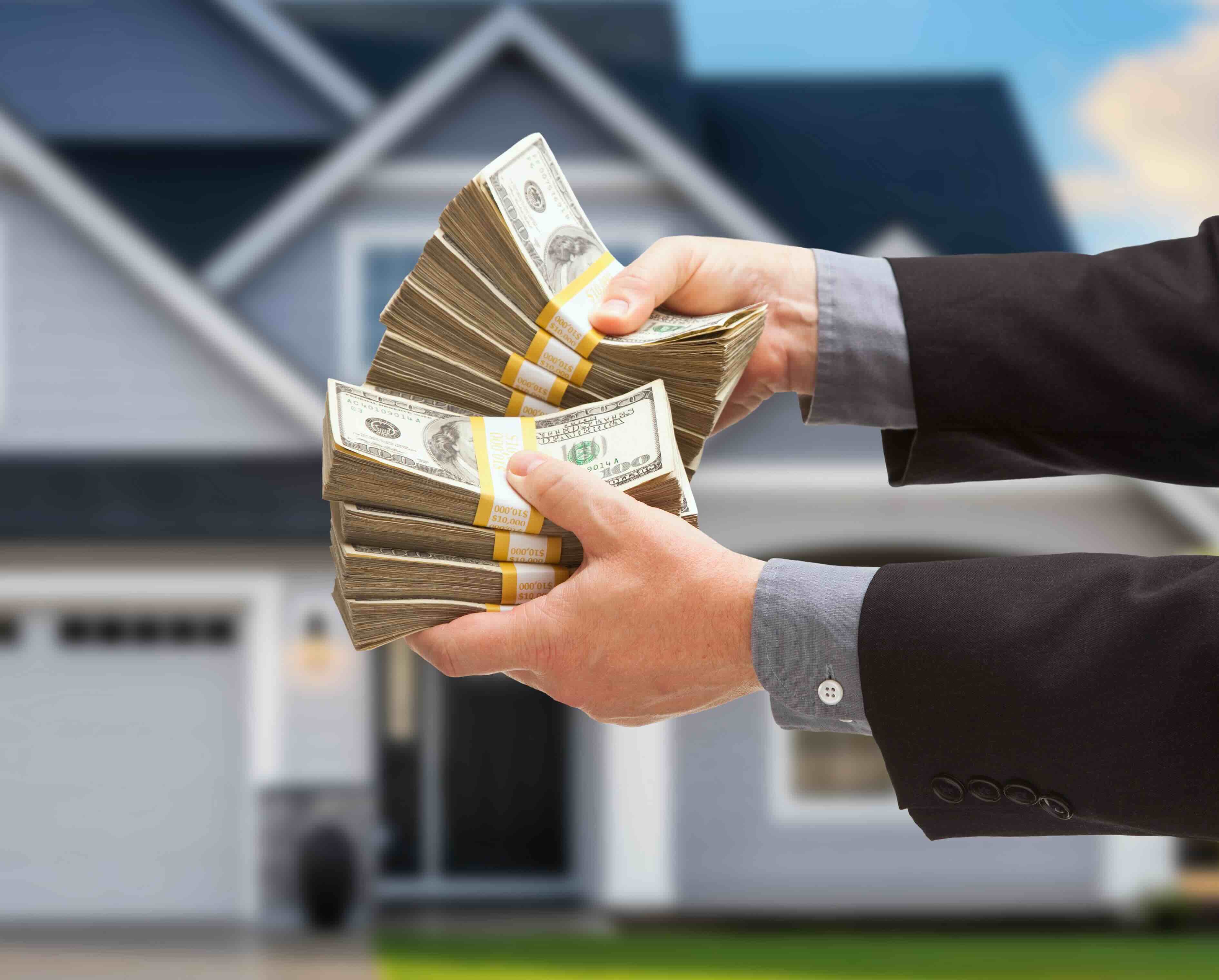 A photo of hands holding cash in front of a house to illustrate an article about realtor vs cash sale transaction.