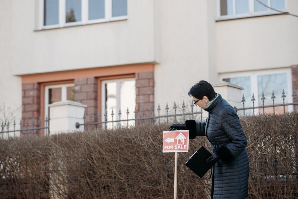 A woman in a black jacket putting for a sale sign.