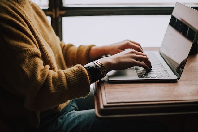 Don't forget to utilize real estate platforms and social media as marketing tools when selling your home solo! Alt text: Person in a yellow sweater typing on a keyboard
