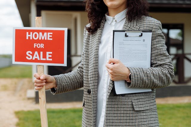 Woman putting a home for sale sign in front of a property