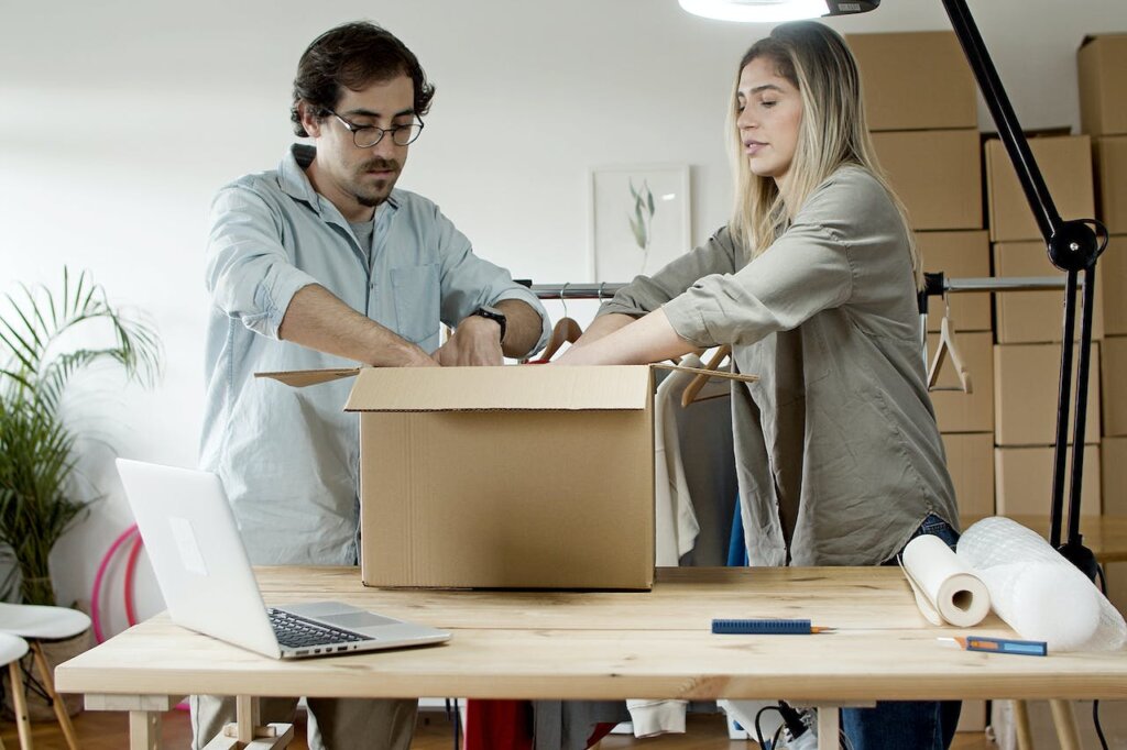 A man and a woman packing a box placed on the desk right next to a laptop