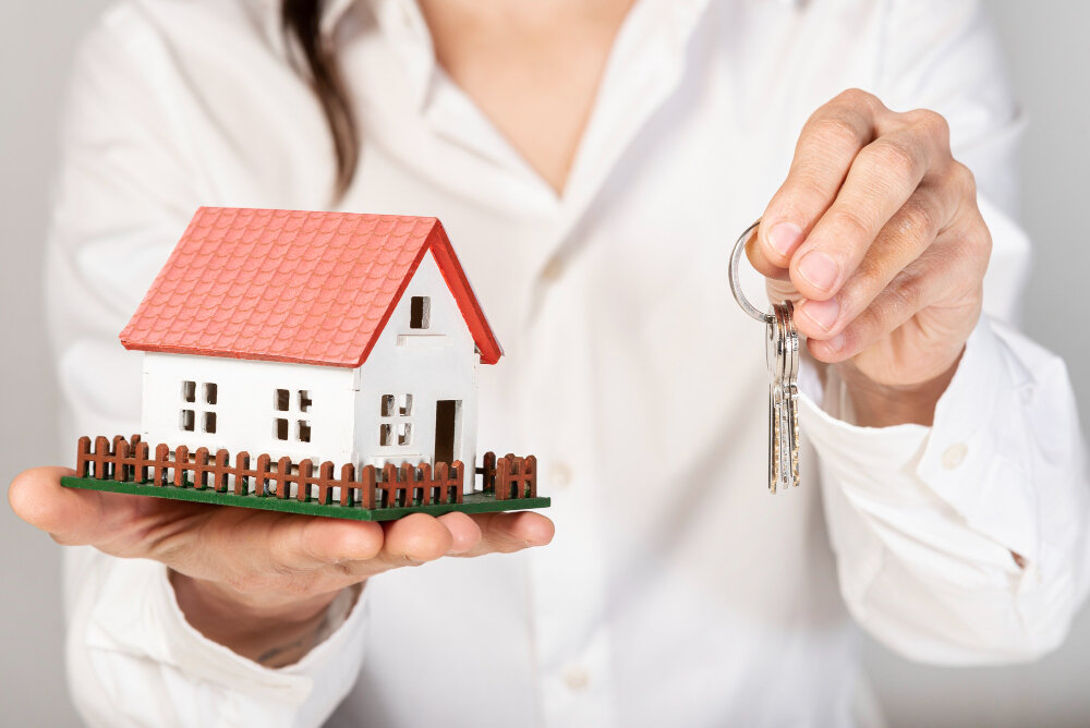 A person holding a miniature house and a set of keys.